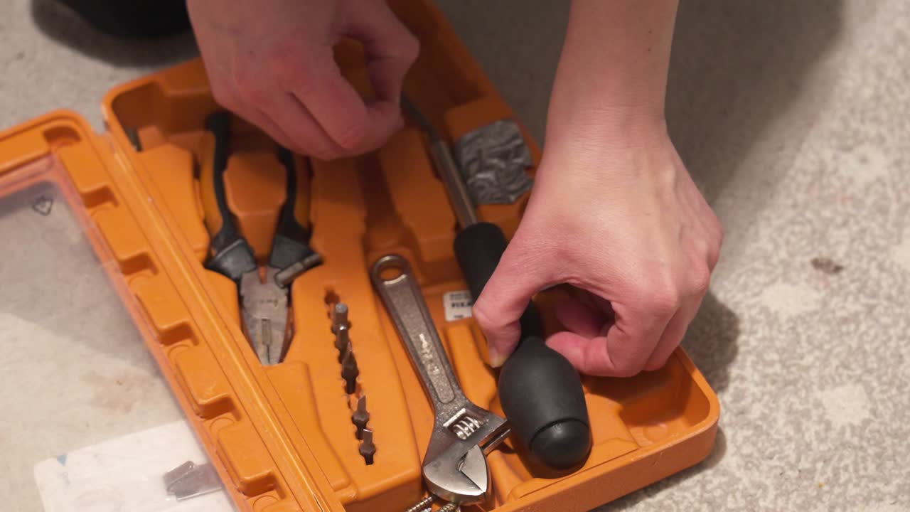 manos organizando herramientas dentro de una caja de herramientas naranja