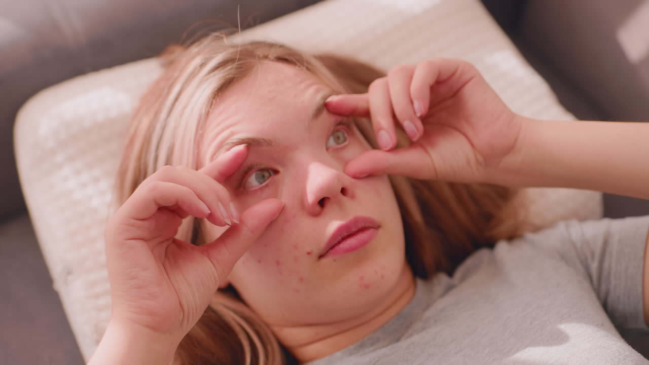 Sleepy girl wakes up lying on couch in soft daylight lazily rubbing eyes with both hands showing morning tiredness and dizziness while adjusting to bright sunlight through window