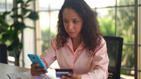 hermosa mujer latina usando un teléfono inteligente con una tarjeta de crédito en la mano