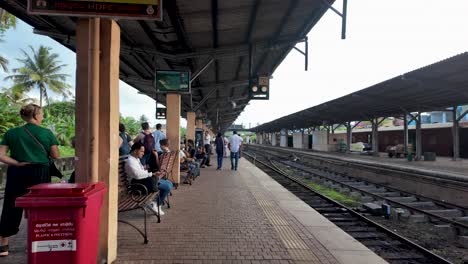 people gathered along the platform of kandy railway station in sri lanka, waiting for trains. the vibrant scene captures daily life and travel in a tropical setting.