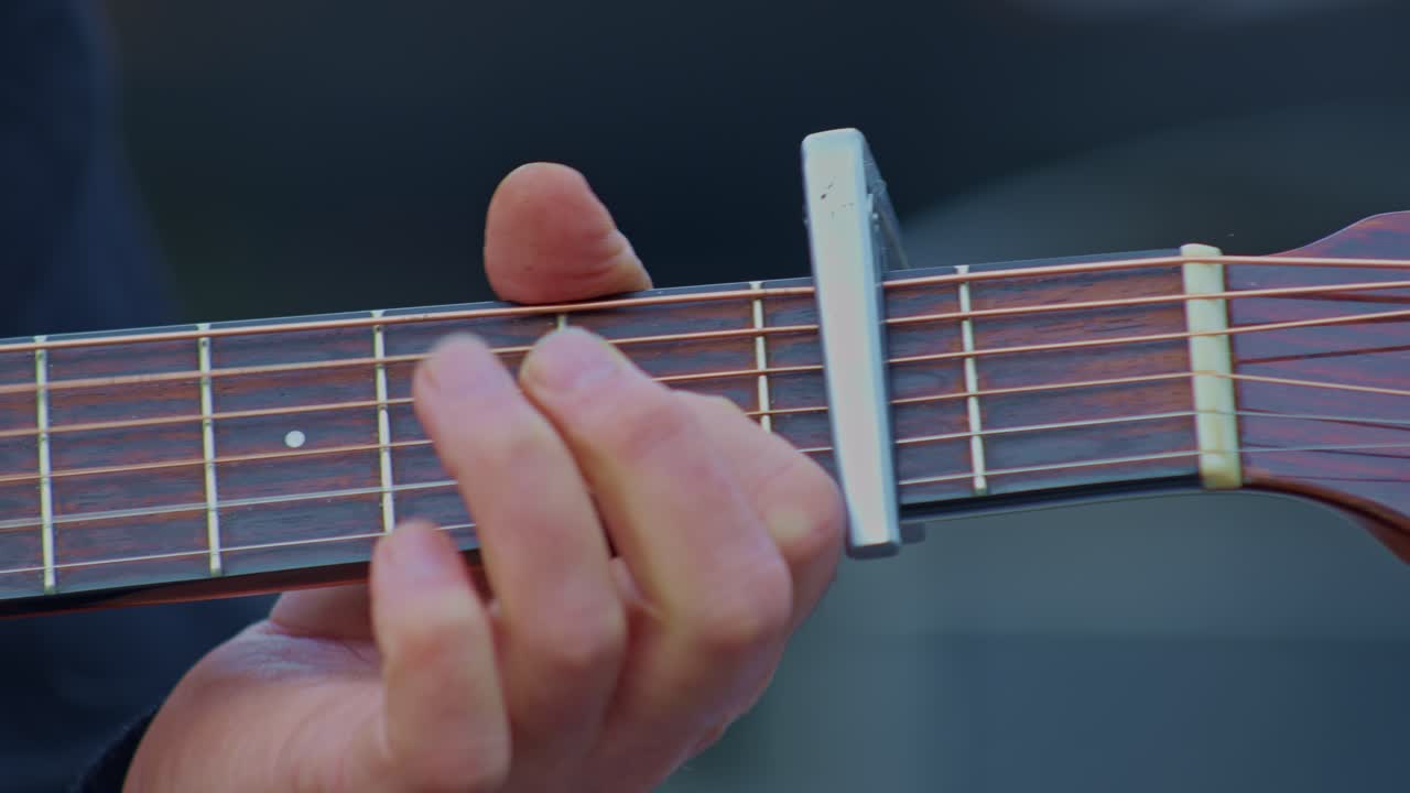 Guitarist plays guitar, super ultra closeup view of hand wrist, fingers, capo, frets and strings