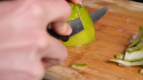 chef hands cutting the skin off a green, juicy lime on a wooden chopping board