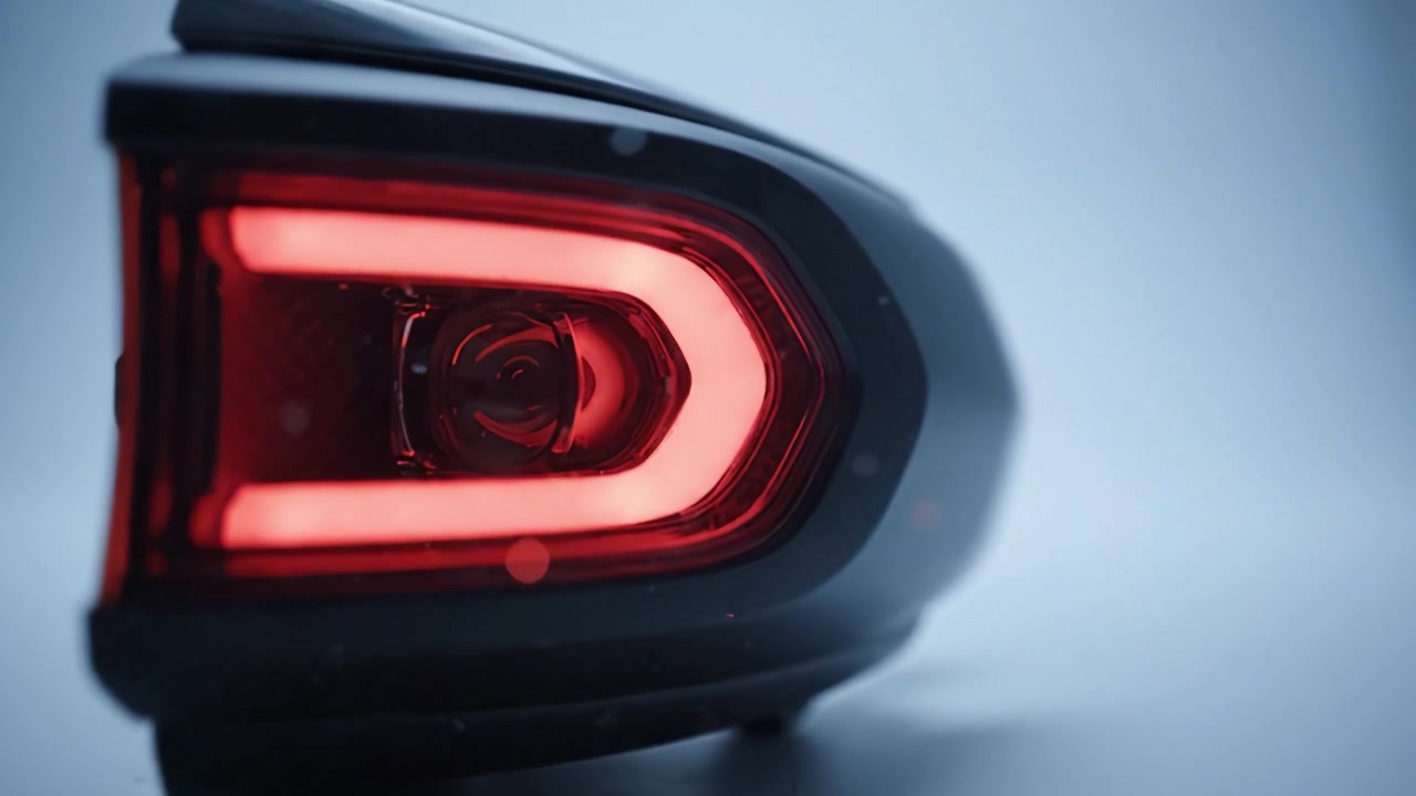 Vue rapprochée d'un feu arrière automobile élégant doté de LED rouges vives et d'un boîtier noir stylé sur un fond bleu doux avec effet bokeh.