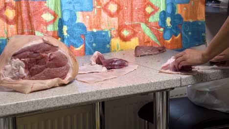 manos de persona cortando carne de cerdo fresca en la cocina doméstica, vista lateral