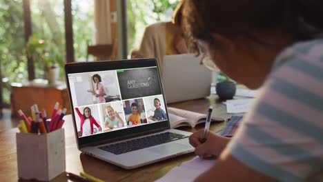 Girl-doing-homework-and-having-a-video-conference-with-teacher-and-classmates-on-laptop-at-home