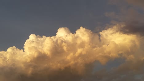 towering cumulus stage clouds illuminated by the sunset, growing and forming taller as a darker clouds passes in front shrouding the view of the rising thunderstorm in the making