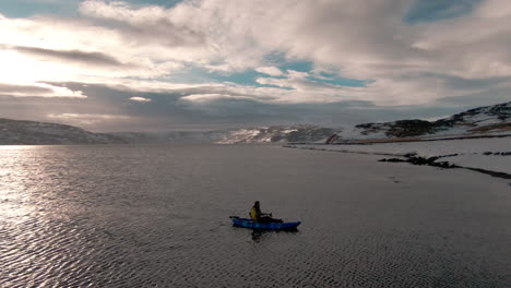 Man-paddling-on-kayak-towards-ocean-shore-at-sunset