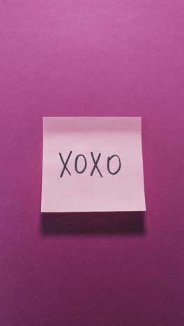 hands posting xoxo sticky note on bright pink wall, capturing affection concept