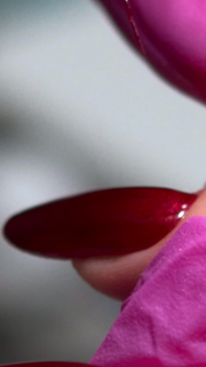 Nærbillede af negletekniker, der påfører gellak på røde, manicurerede negle