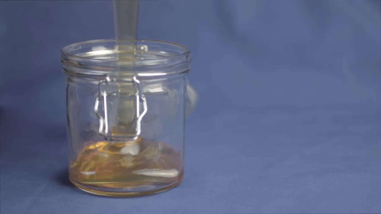 Golden runny honey pouring into a jar wide shot on blue background