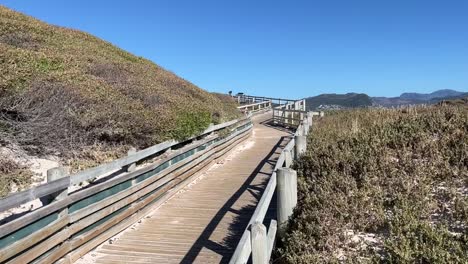un paseo marítimo de madera que conduce a la playa de las rocas cerca de la ciudad de simons, sudáfrica, el muelle conduce a través de dunas de arena cubiertas de cepillos