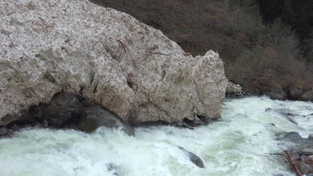 Fiume di montagna impetuoso che scorre accanto a un grande banco di neve