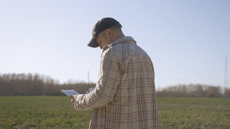 Caucasian-man-in-plaid-shirt-watching-something-on-a-tablet-and-looking-around-in-the-countryside