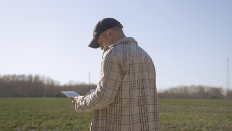 ein kaukasischer mann in kariertem hemd, der etwas auf einem tablet beobachtet und auf dem land herumblickt