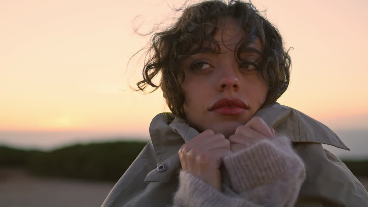 클로즈업 아름다운 소녀 해가 지는 하늘, 꿈꾸는 곱슬한 여자가 추운 저녁에 따뜻해지다