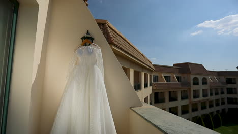 The-bride's-dress-hanging-on-a-wall-in-the-hotel's-garden-in-the-morning---push-in