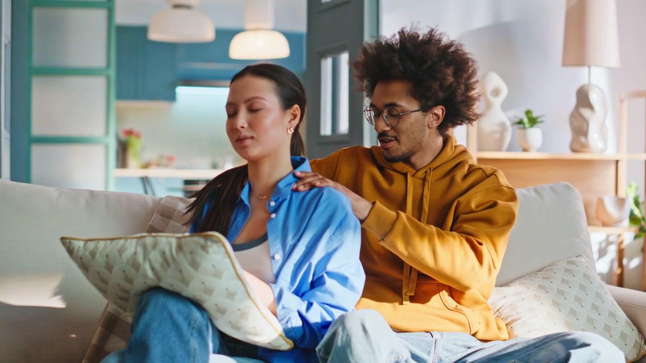 Boyfriend giving girlfriend shoulder massage on sofa. Couple relaxing at home.