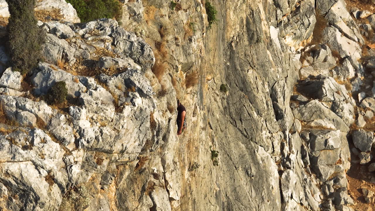 Telephoto drone shot revealing a rock climber on a steep mountain wall, sunrise