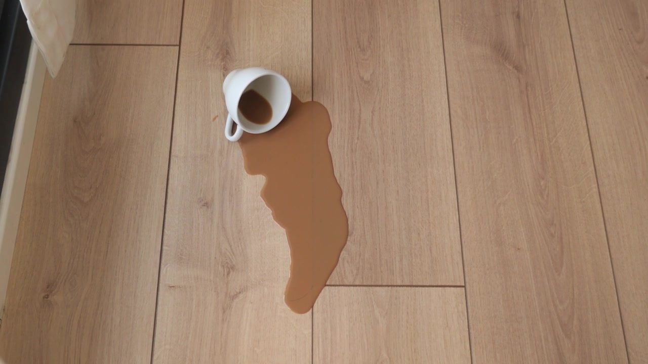Kaffe spildt fra en hvid kop ned på et trægulv