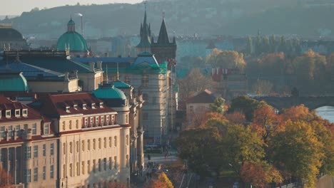 una mañana tranquila en praga con edificios históricos, cúpulas verdes, puentes y árboles de colores de otoño a la vista.