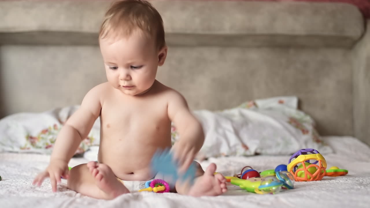 Caucasian blonde baby boy on a bed, playing with toys. Slow motion
