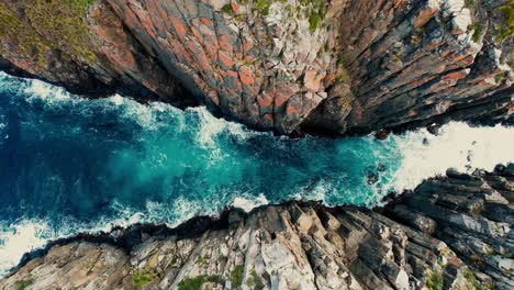 cape hauy drone flys down in between cliffs in tasmania, australia