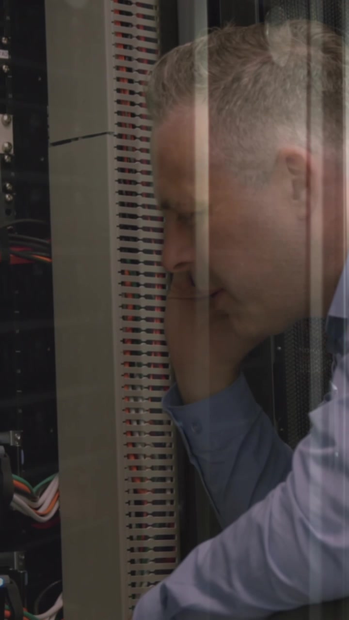Caucasian senior male engineer talking on smartphone while working in computer server room