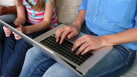 una madre y su hija descansando en el sofá y usando una computadora portátil