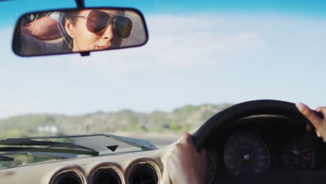mujer afroamericana conduciendo por una carretera de campo en un coche descapotable