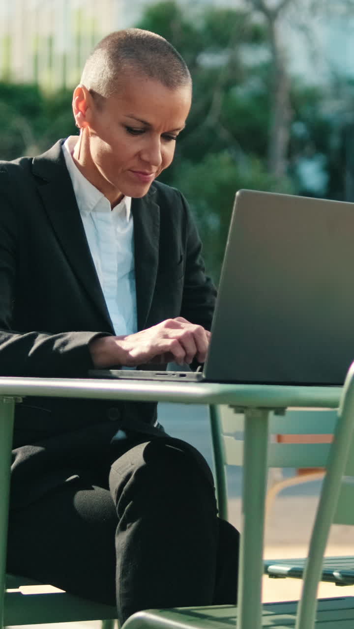 Donna concentrata che lavora al portatile a un tavolo di un bar all'aperto