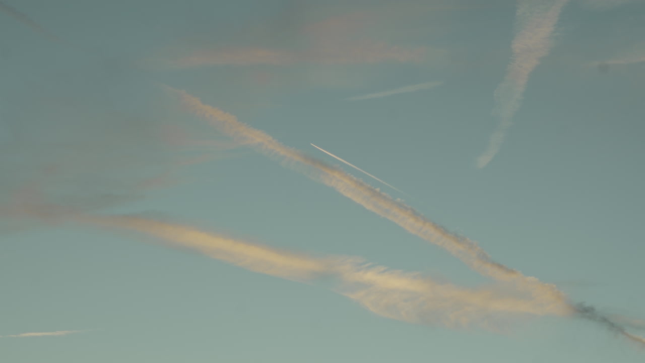 Solnedgangshimmel med skyer og kondensstriber fra fly om sommeren