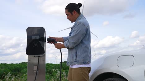 progressive man with his ev car and wind turbine as concept of renewable energy.