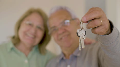 verschwommenes älteres paar, das in die kamera lächelt und die schlüssel ihres neuen hauses zeigt