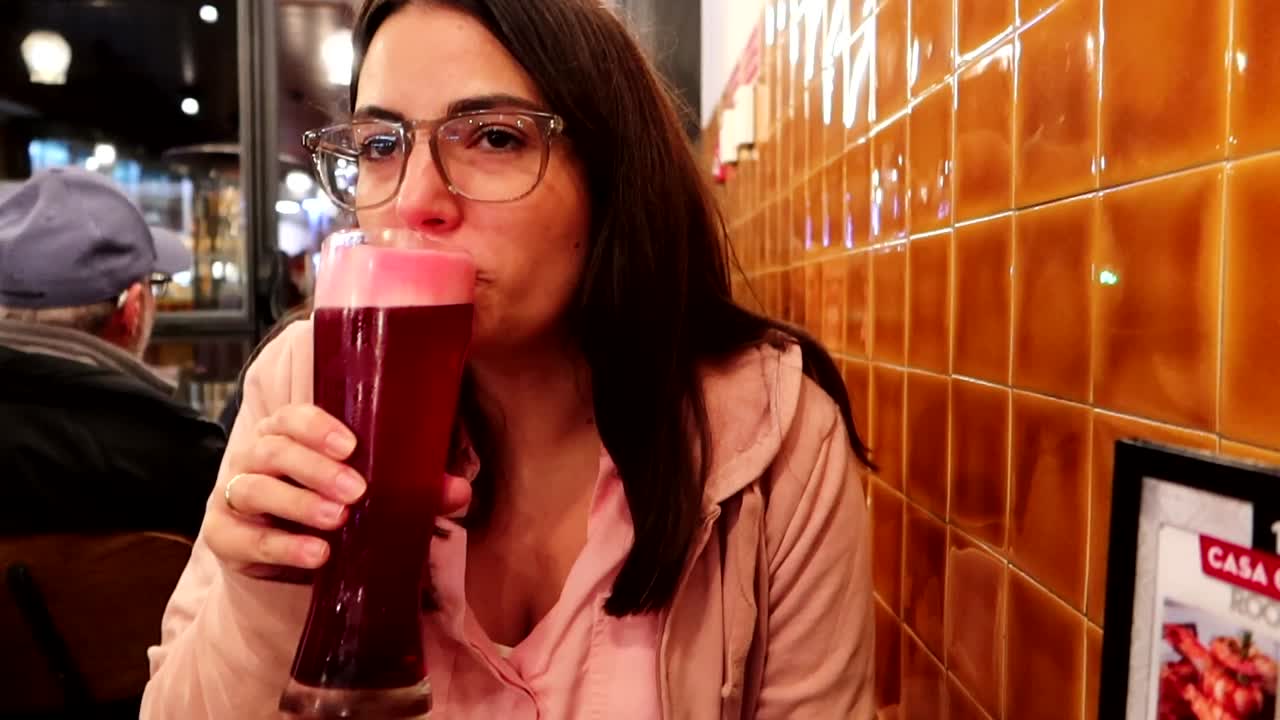 imágenes en cámara lenta de una mujer saboreando cerveza roja en un bar animado por la noche