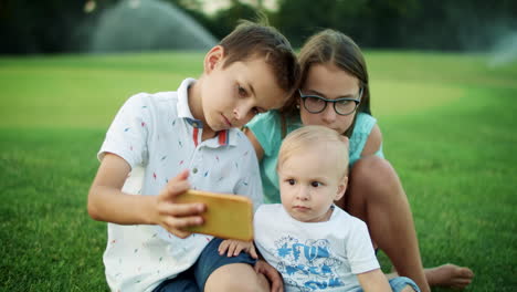 niños centrados sentados en la hierba en el prado. niño lindo tomando una selfie en el teléfono celular