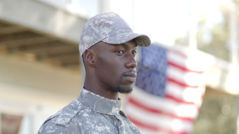 un soldado afroamericano serio de pie con una bandera en el fondo en un día soleado, en cámara lenta