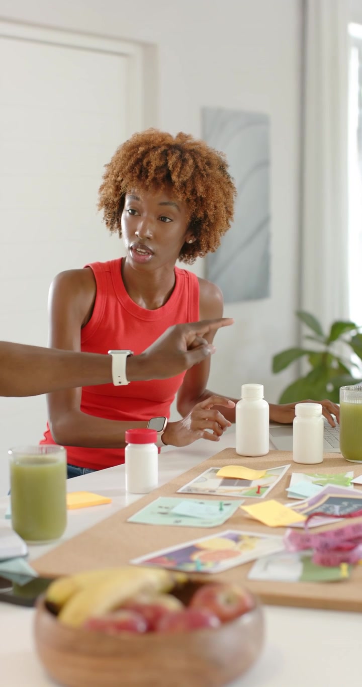 Vertical video: African duo arranging bottles, tapping laptop at table after offscreen cue planning