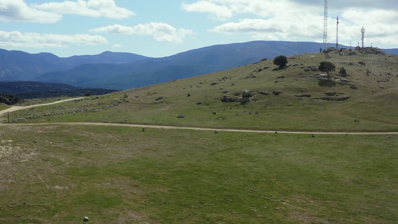 vuelo frontal sobre una pequeña colina cubierta de hierba con antenas repetidoras de señal en una zona rural rodeada de montañas en el barraco, ávila, españa, en un soleado día de invierno.