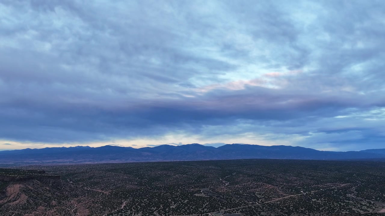 En filmatisk dronetimelapse fanger falmende lys og skiftende farger på et skylag over en robust fjellkjede i sørvest. Denne dramatiske kveldsovergangen gir en naturskjønn naturbakgrunn.