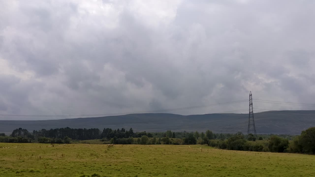 brecon beacons wales uk 4k의 전기 철탑과 극적인 산악 풍경을 배경으로 들판에서 풀을 뜯고 있는 양의 패닝 샷
