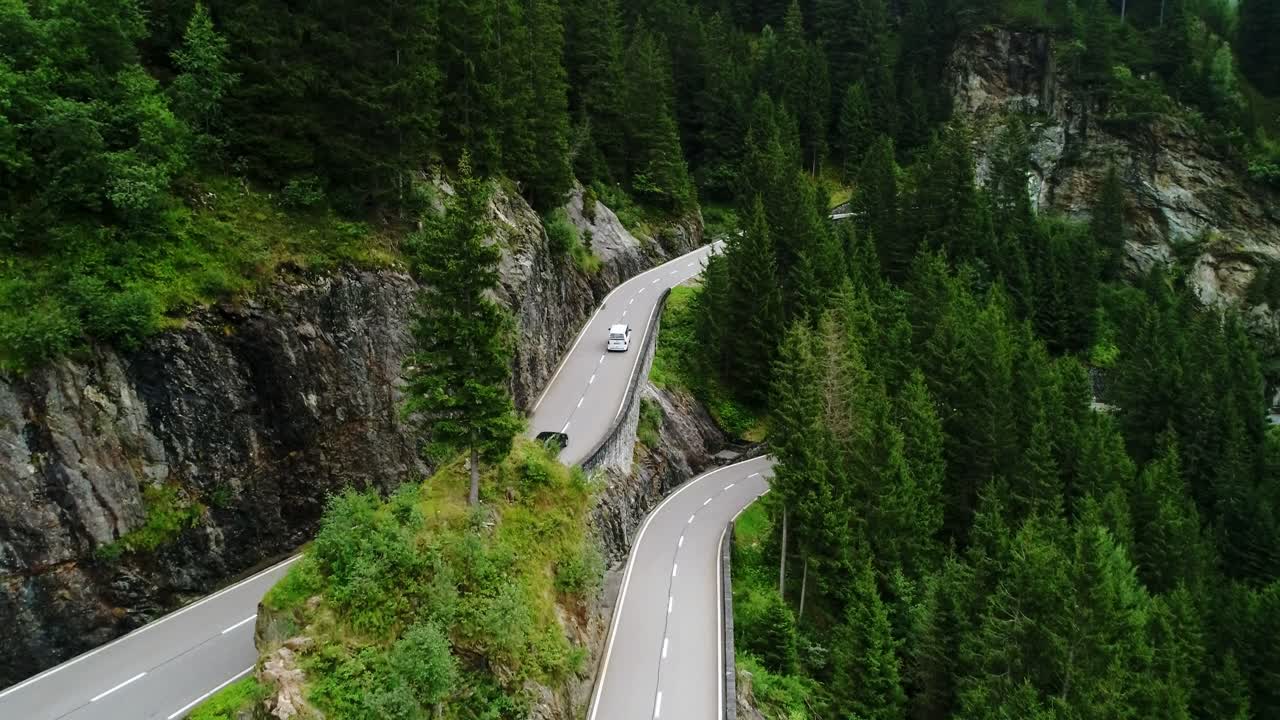 Winding road cuts through Grimsel Pass, surrounded by Swiss Alps and forests