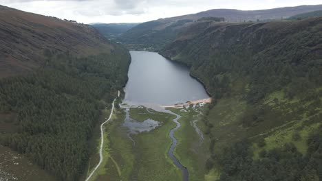 vista panorámica del lago superior de glendalough rodeado por el exuberante bosque verde y las montañas en el condado de wicklow, irlanda