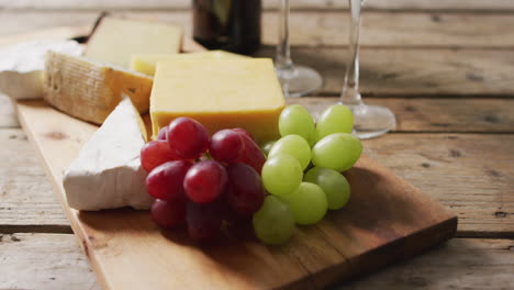 Video-of-diverse-cheeses,-grapes-and-glasses-of-wine-on-wooden-surface