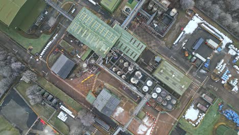 cinematic overhead drone aerial footage of a large industrial plant showing pipework structures, buildings, cooling towers, steam, and work vehicles