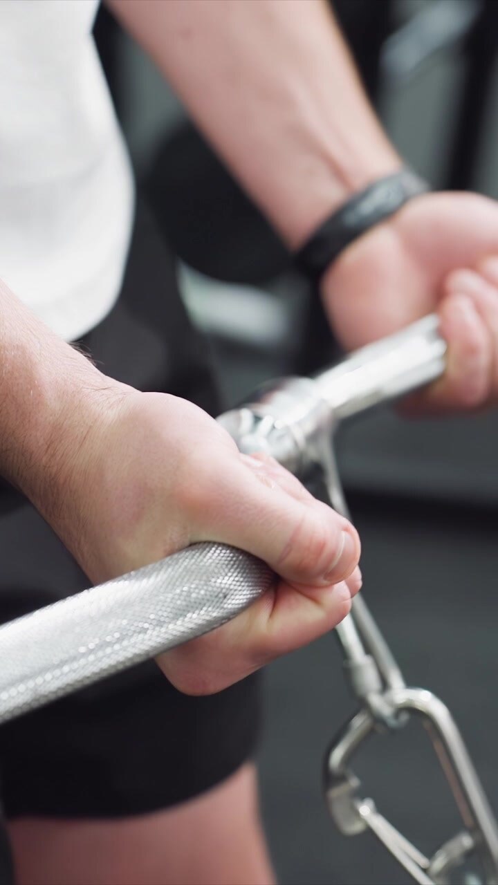 Close up view shows hands gripping weights during exercise emphasizing grip technique. focus remains on interaction between hand and barbell with weight plates visible in motion indicating