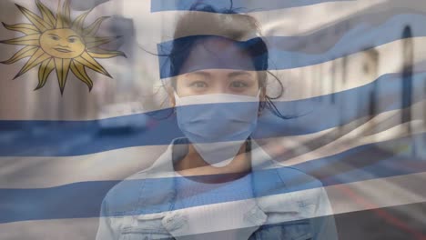 Animation-of-flag-of-uruguay-waving-over-woman-wearing-face-mask-during-covid-19-pandemic