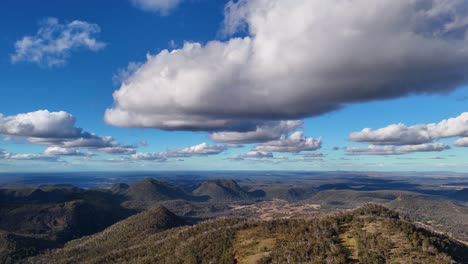 aerial drone footage smoothly pans over the rugged warrumbungle mountain range under dramatic clouds and bright daylight, revealing vast australian wilderness and rolling hills