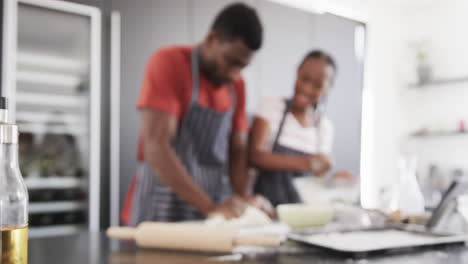 Happy-african-american-couple-in-aprons-baking-together,-kneading-dough-in-kitchen,-slow-motion