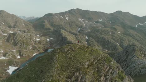 Luftaufnahme-Eines-Mannes,-Der-über-Einen-Berghügel-Wandert,-Mit-Einem-Wunderschönen-Blauen-Bergsee,-Der-In-Der-Ferne-Innerhalb-Der-Alpen-Sichtbar-Ist