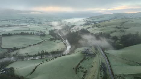 fog shrouded landscape with meandering river amongst patchwork fields at dawn in winter